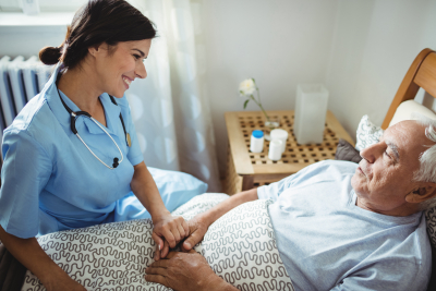 Nurse holding hands of elderly man in bed